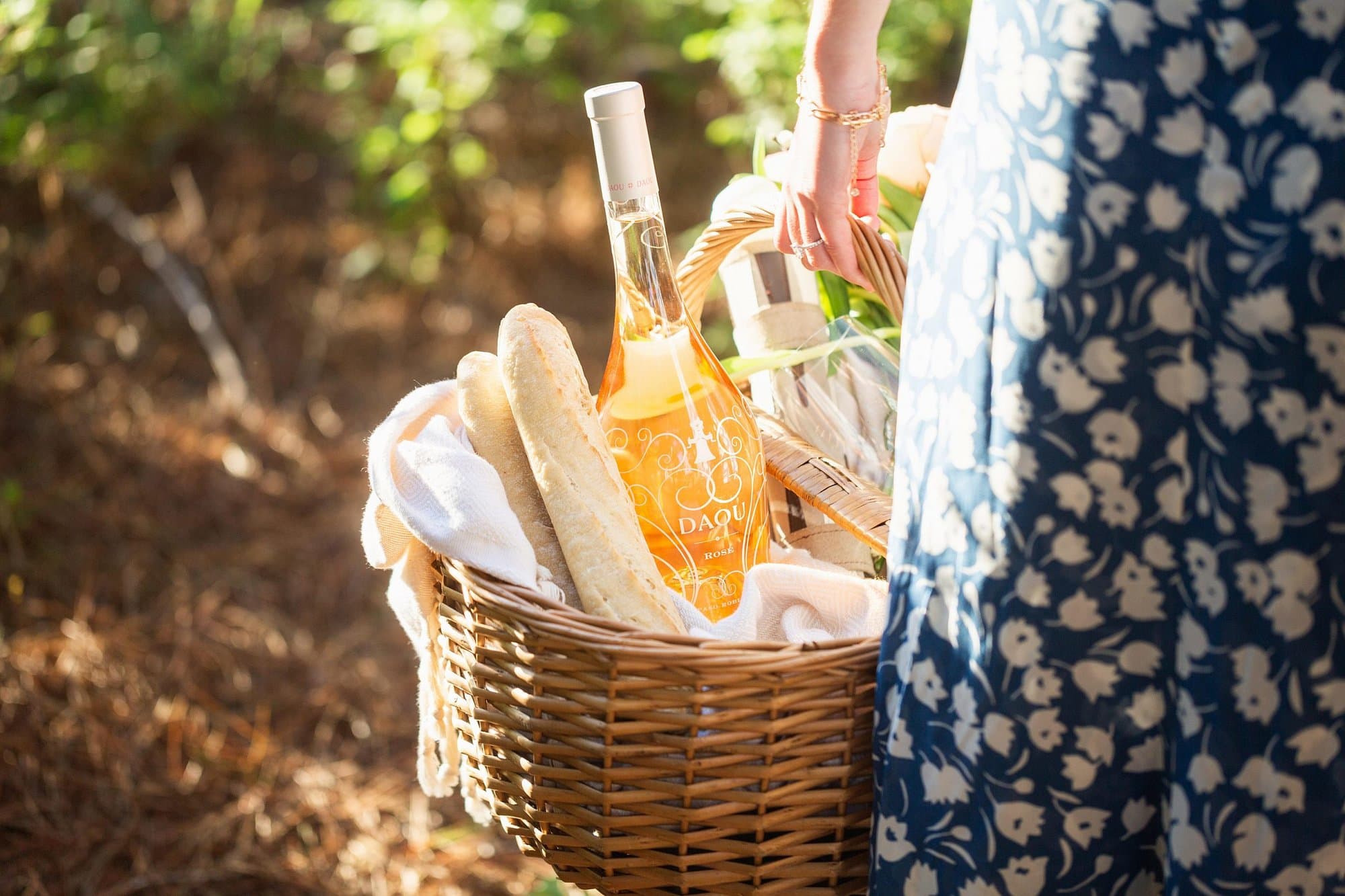 A woman carries a picnic basket with loaves of baguette and a bottle of DAOU rosé